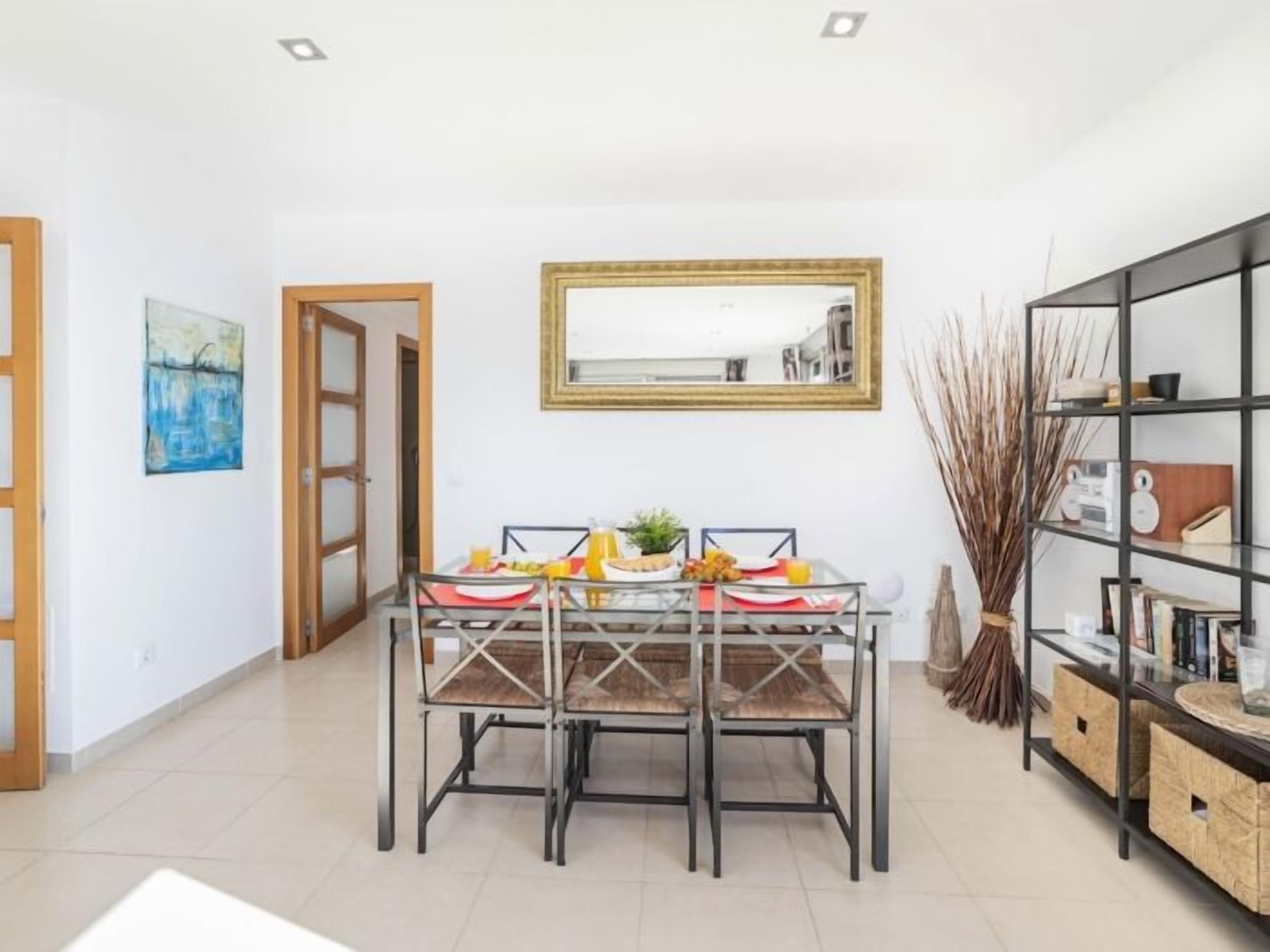 A dining area with a table and chairs, a mirror above, and a bookshelf to the side.