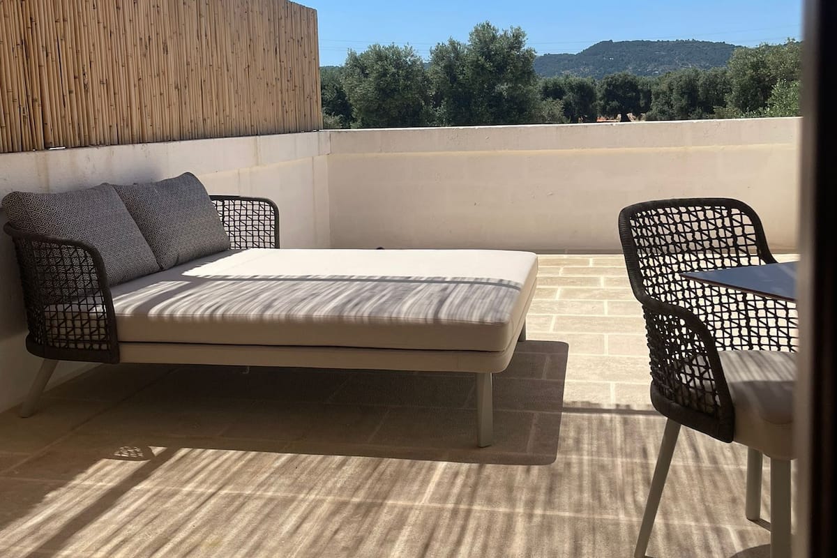 Ein Balkon mit einem Bett, zwei Stühlen und Blick auf die Landschaft.