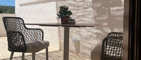 A patio with two chairs and a table, a potted plant, and a white wall.