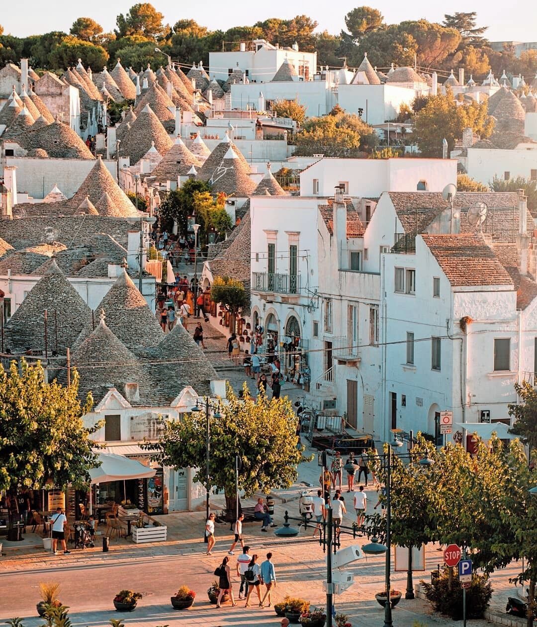 A town with white buildings and conical roofs, a central square with people, and a stop sign.