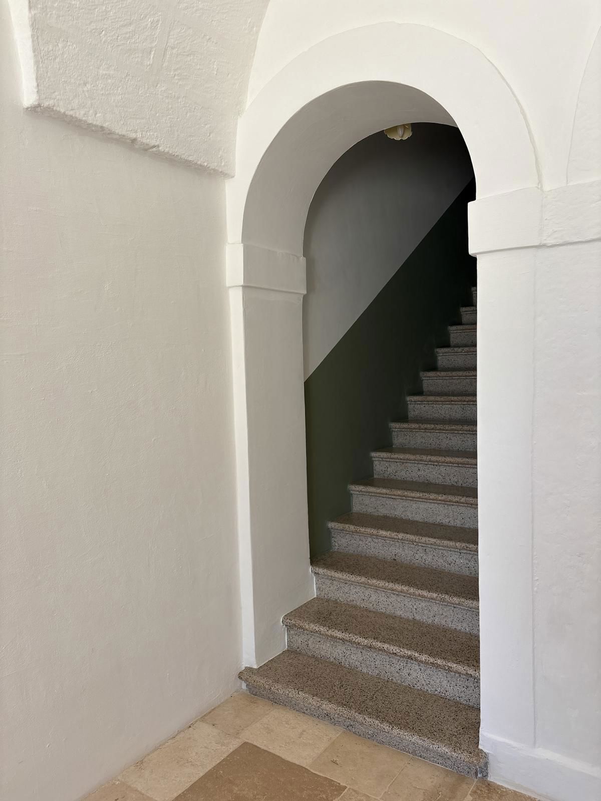A staircase with a white archway leading to a dark staircase.