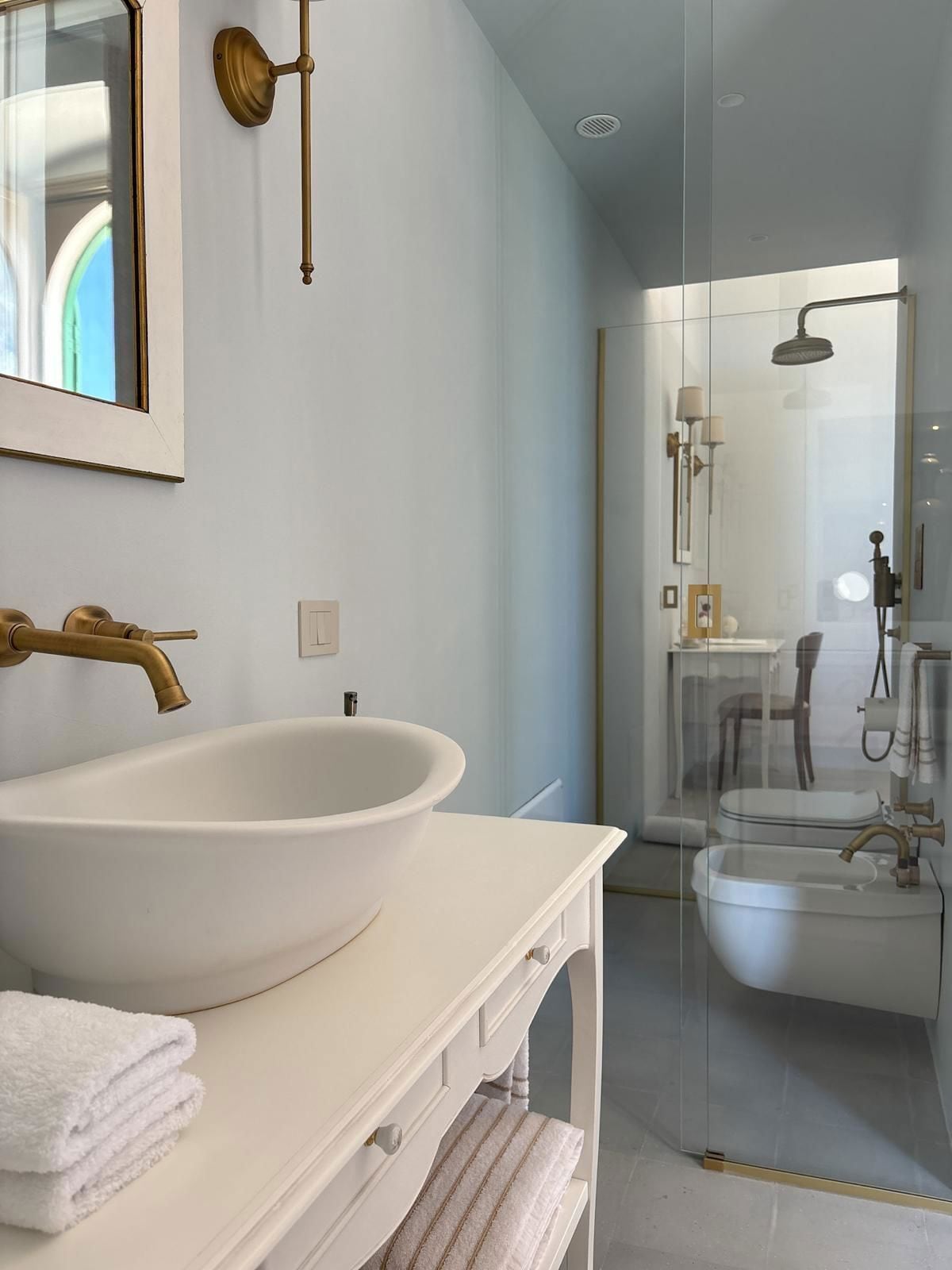 Un baño moderno con un lavamanos grande blanco, un grifo dorado y una cabina de ducha de vidrio.