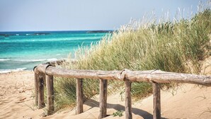 A sandy beach with a wooden fence and tall grass in the foreground.