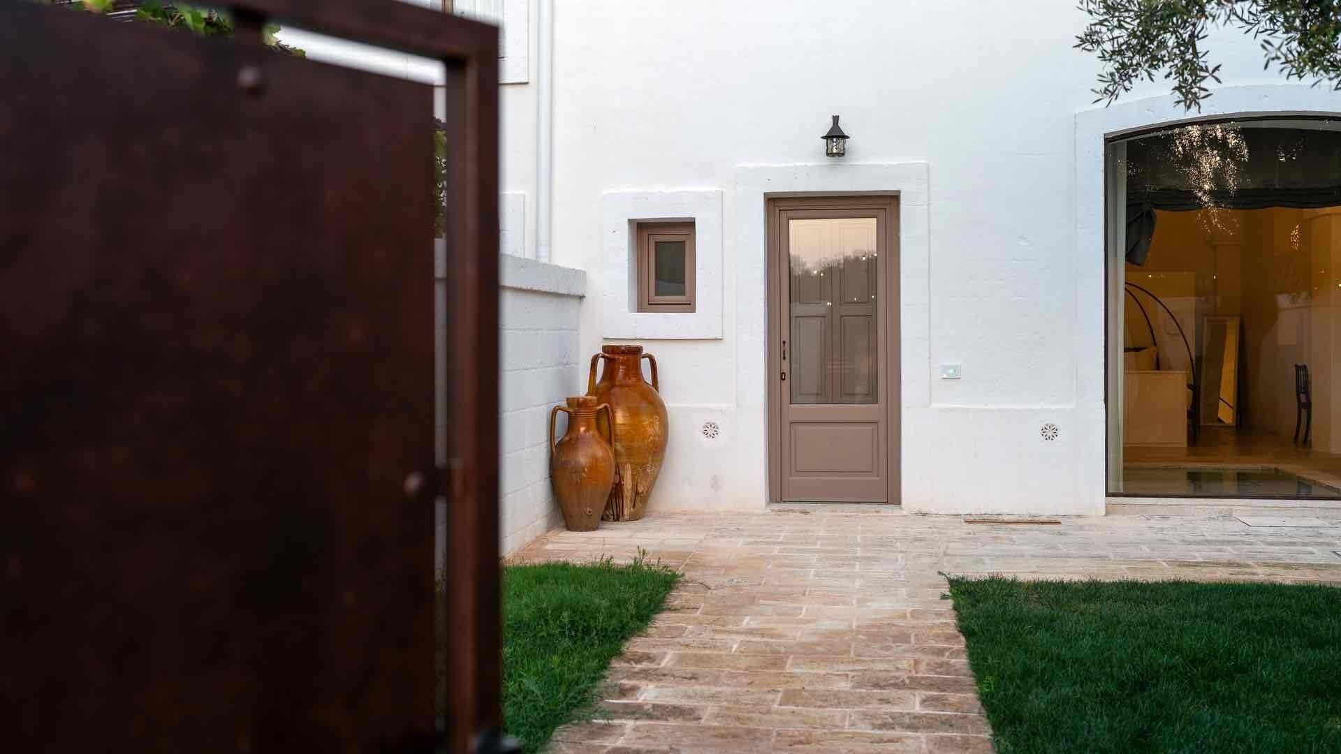A white building with a brown door, a small window, and two large vases on the ground.