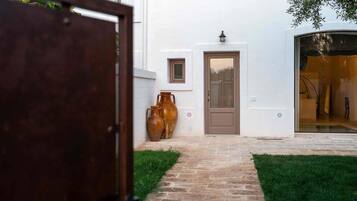A white building with a brown door, a small window, and two large vases on the ground.