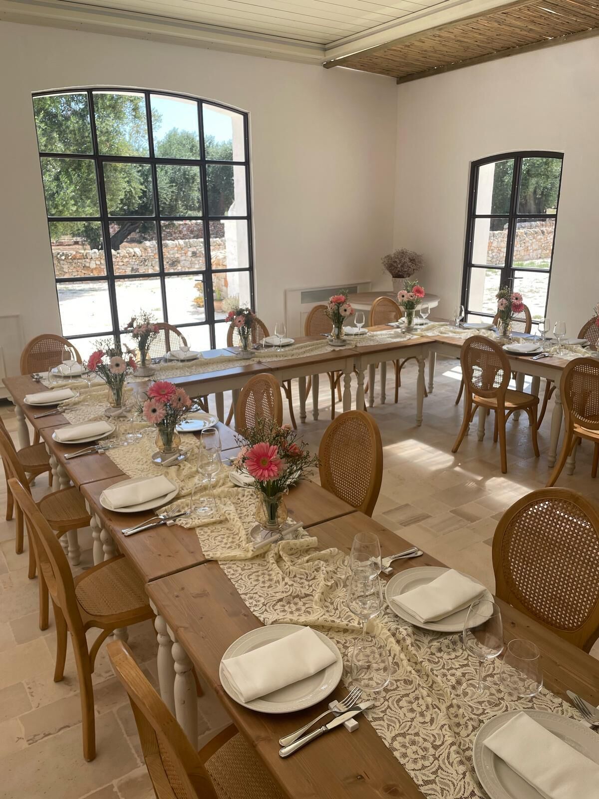 Comedor con una larga mesa de madera dispuesta para una comida, amplias ventanas con vistas a zonas verdes y sillas de mimbre.