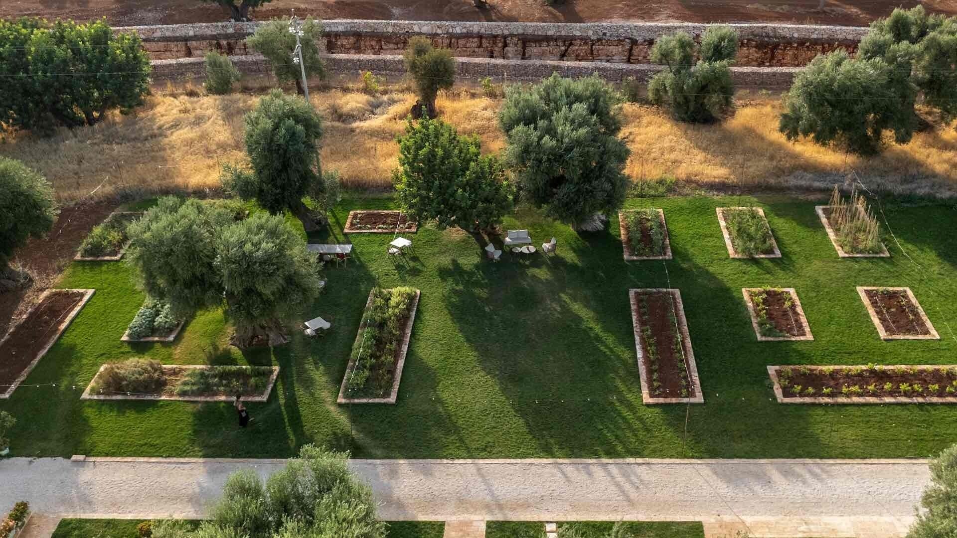 An aerial view of a landscaped garden with rectangular flower beds, trees, and a paved walkway.