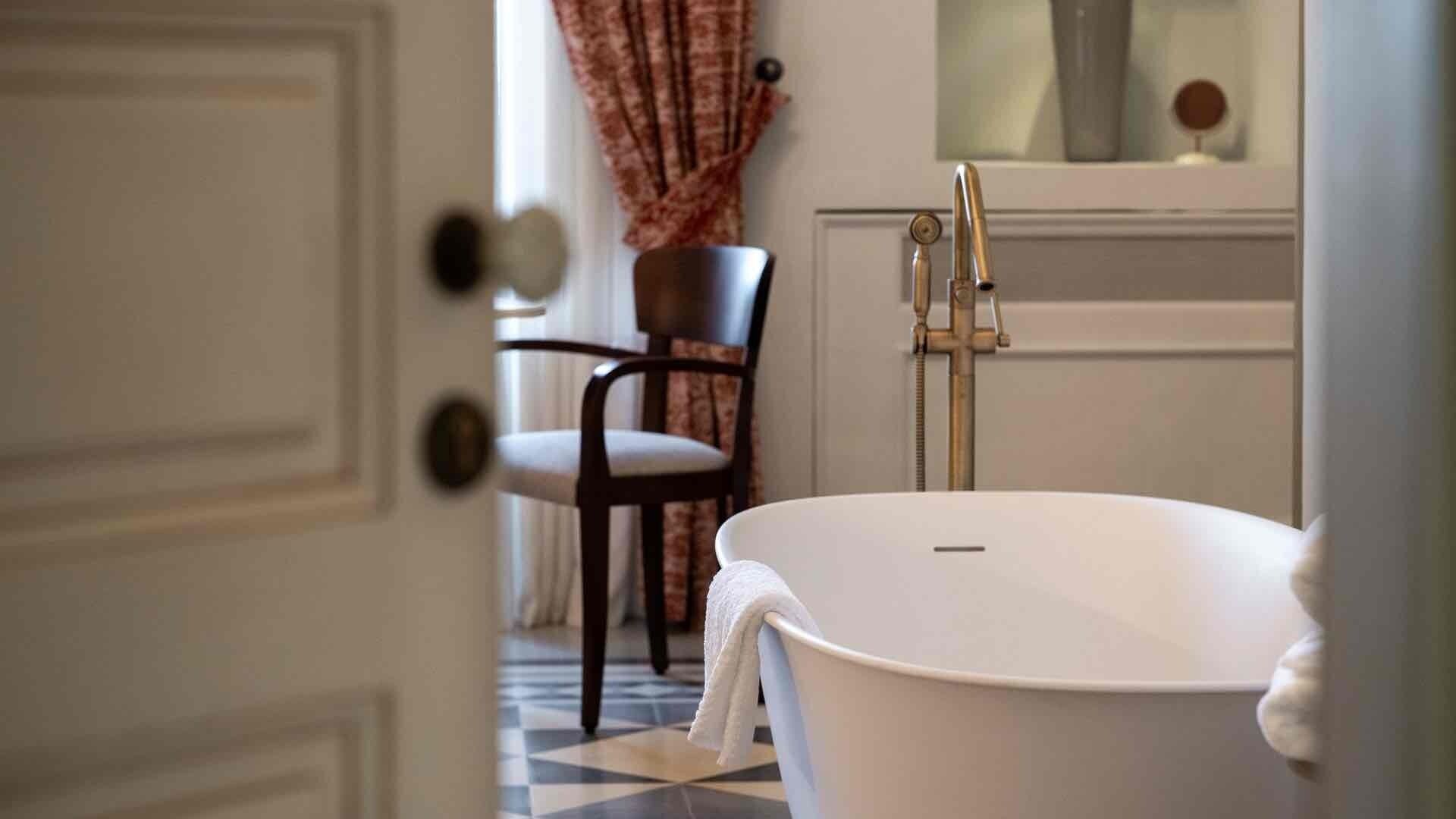 A bathroom with a freestanding bathtub, a chair, and a door with a round doorknob.