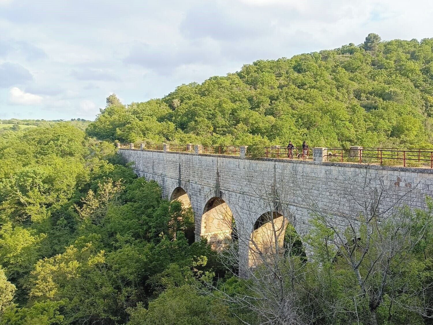 A stone bridge with multiple arches over a lush green valley.