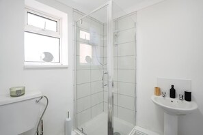 Une salle de bain avec une douche en verre, une fenêtre, un lavabo avec des articles de toilette et des toilettes.