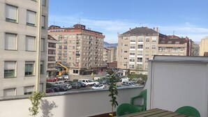 Une terrasse sur le toit, avec une table et des chaises, un pot de fleurs et une vue sur les bâtiments environnants et les voitures garées.