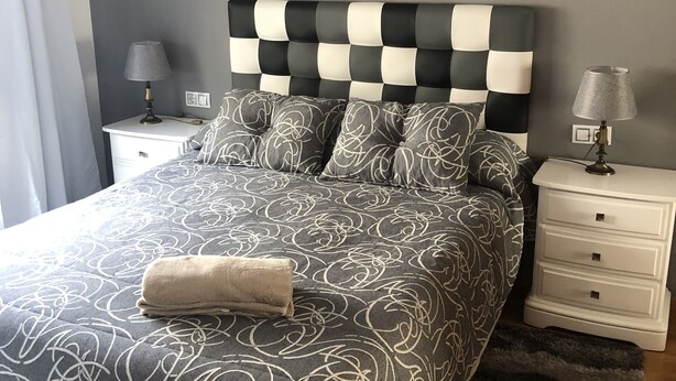Une chambre à coucher bien rangée, avec une tête de lit à carreaux, une couvre-lit à motifs et deux tables de chevet dotées de lampes.