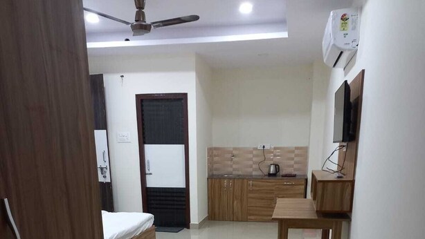 A modern, well-lit room with a bed, a wooden table, and a kitchenette area. - Tirath Hotel - Rishikesh - Uttrakhand (Rishikesh)