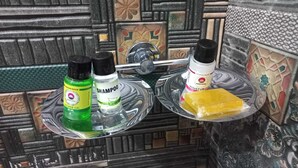 A bathroom with a tiled wall, a shower area, and toiletries on a tray. - Tirath Hotel - Rishikesh - Uttrakhand (Rishikesh)