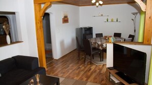 A living room with a black sofa, a TV, and a dining area with a table and chairs.
