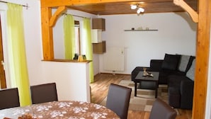 A cozy room with a wooden ceiling, a dining table with chairs, a black sofa, and a small table with a lamp.