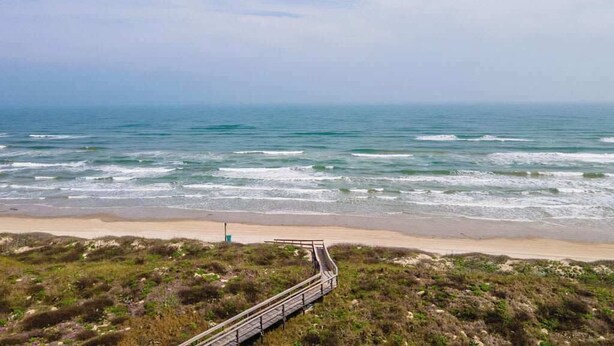 A coastal view with a sandy beach, a wooden boardwalk, and the ocean.