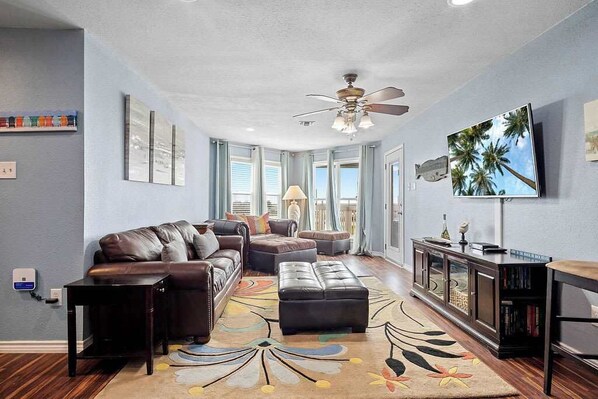 A living room with a sofa, ottoman, and a television on a stand.