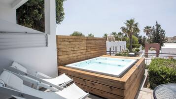 Terraza en la azotea con jacuzzi, sillones blancos para lounge y una cubierta de madera.