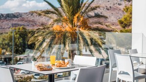 A dining area with a table set for breakfast, including croissants, juice, and coffee, overlooking a mountainous landscape with palm trees. - Aiora Aqua Resort (Rhodes)