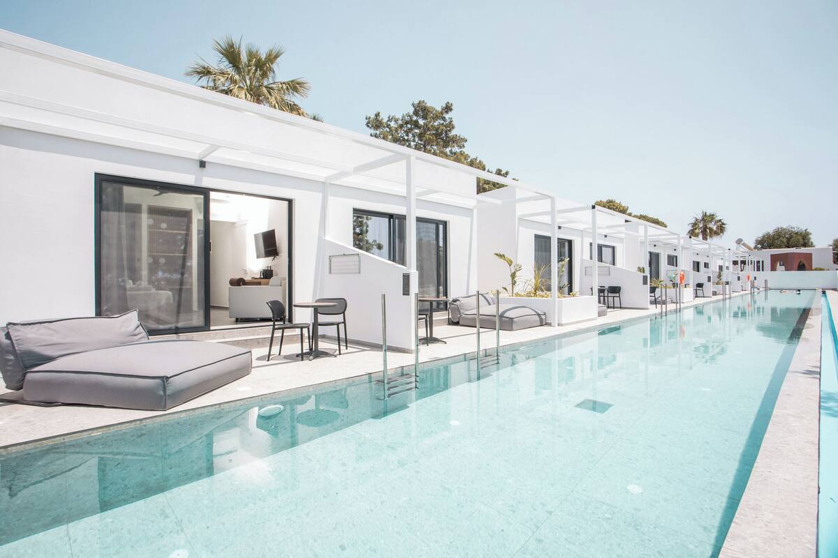 A modern hotel with a long swimming pool, outdoor seating, and a clear view of the surrounding area.