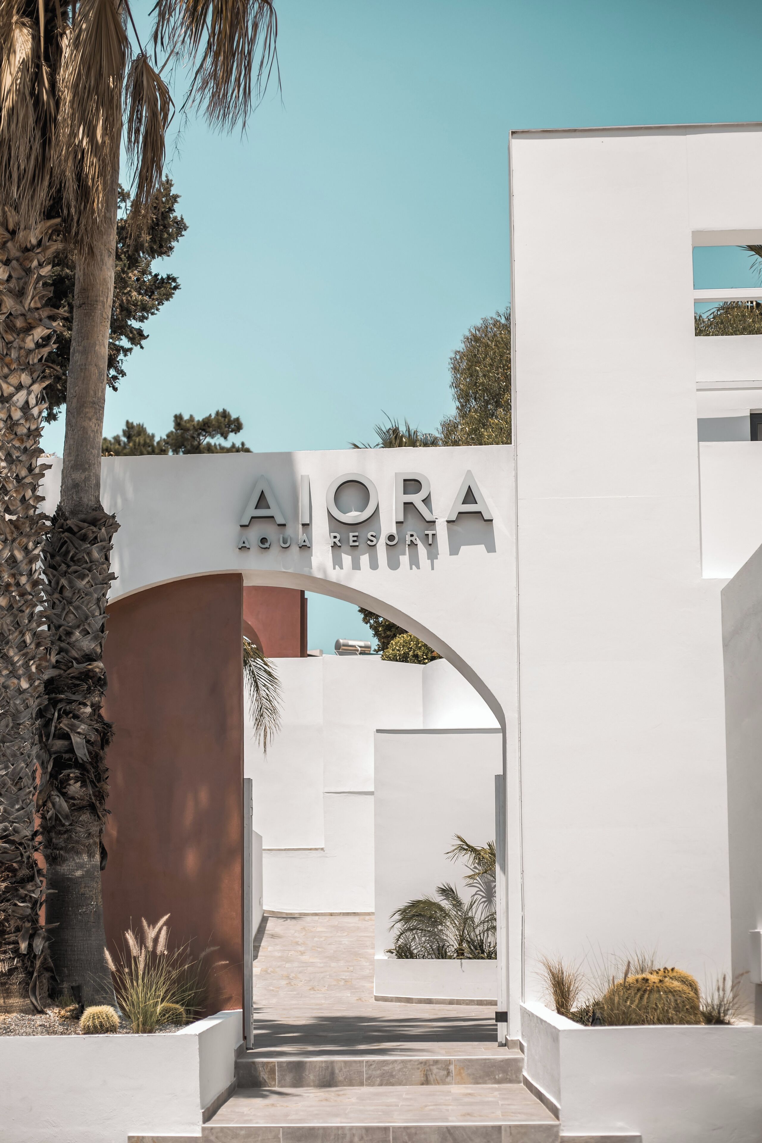 A modern building entrance with the sign "AIORA AQUA RESORT" and a pathway leading to the entrance.