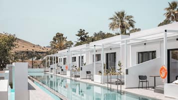Un área moderna junto a la piscina con una pileta larga, estructuras blancas y palmeras al fondo.
