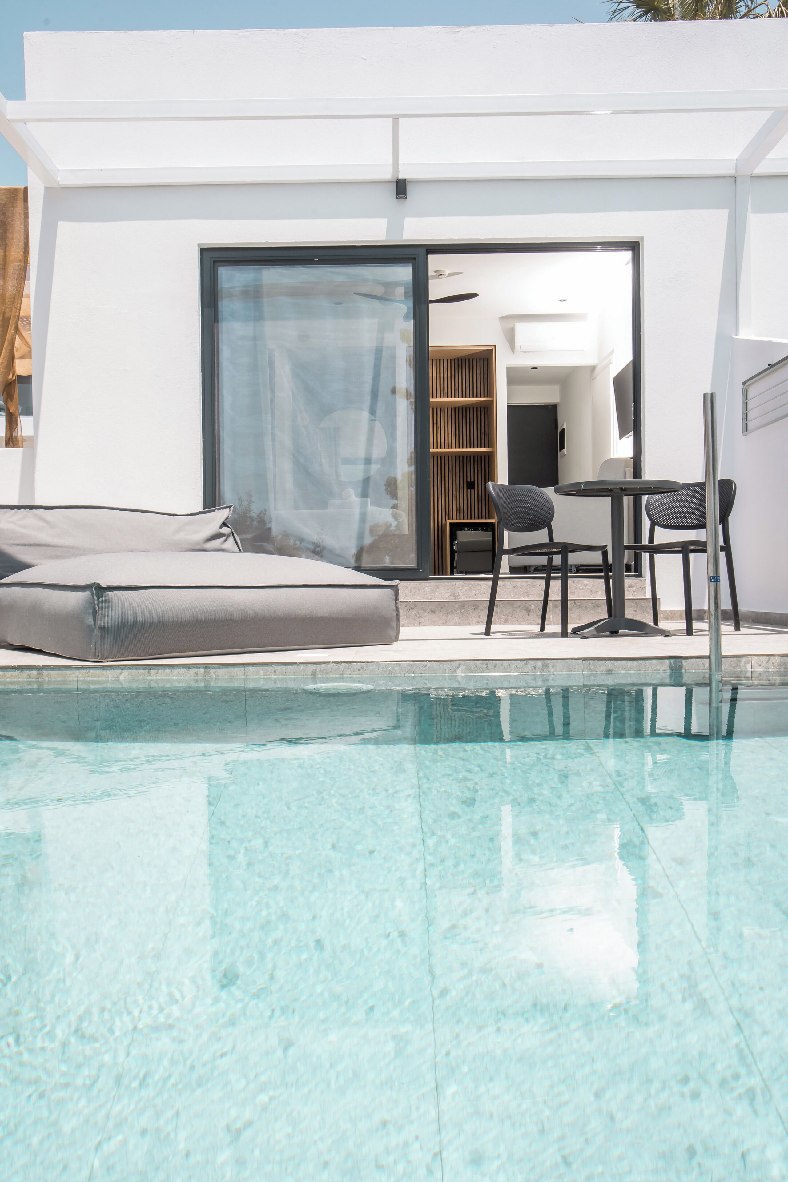 A modern pool area with a glass enclosure, a sofa, and a table with chairs.