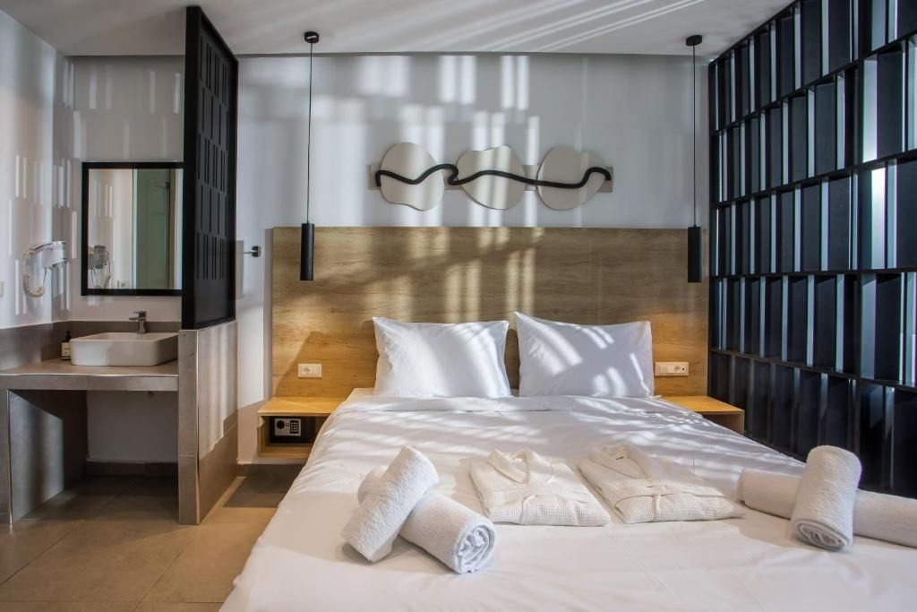Una habitación de hotel moderna con una cama grande, cabecera de madera, escritorio empotrado con lavamanos y un ventanal con persianas.