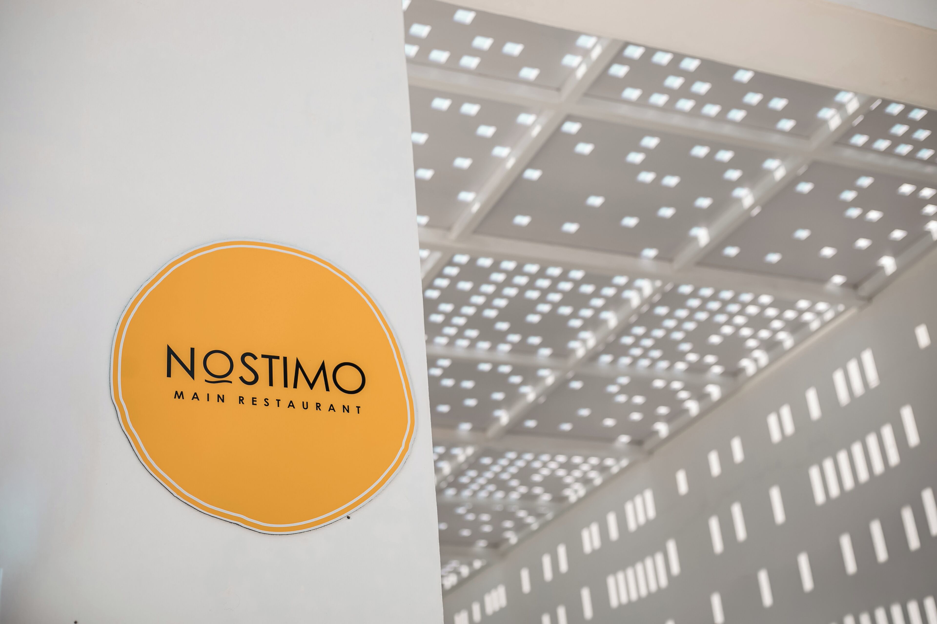 Une enseigne avec l’inscription « NOSTIMO MAIN RESTAURANT » sur un mur blanc.