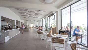 Un comedor espacioso y moderno con ventanas amplias, mobiliario blanco y una zona de cocina central.