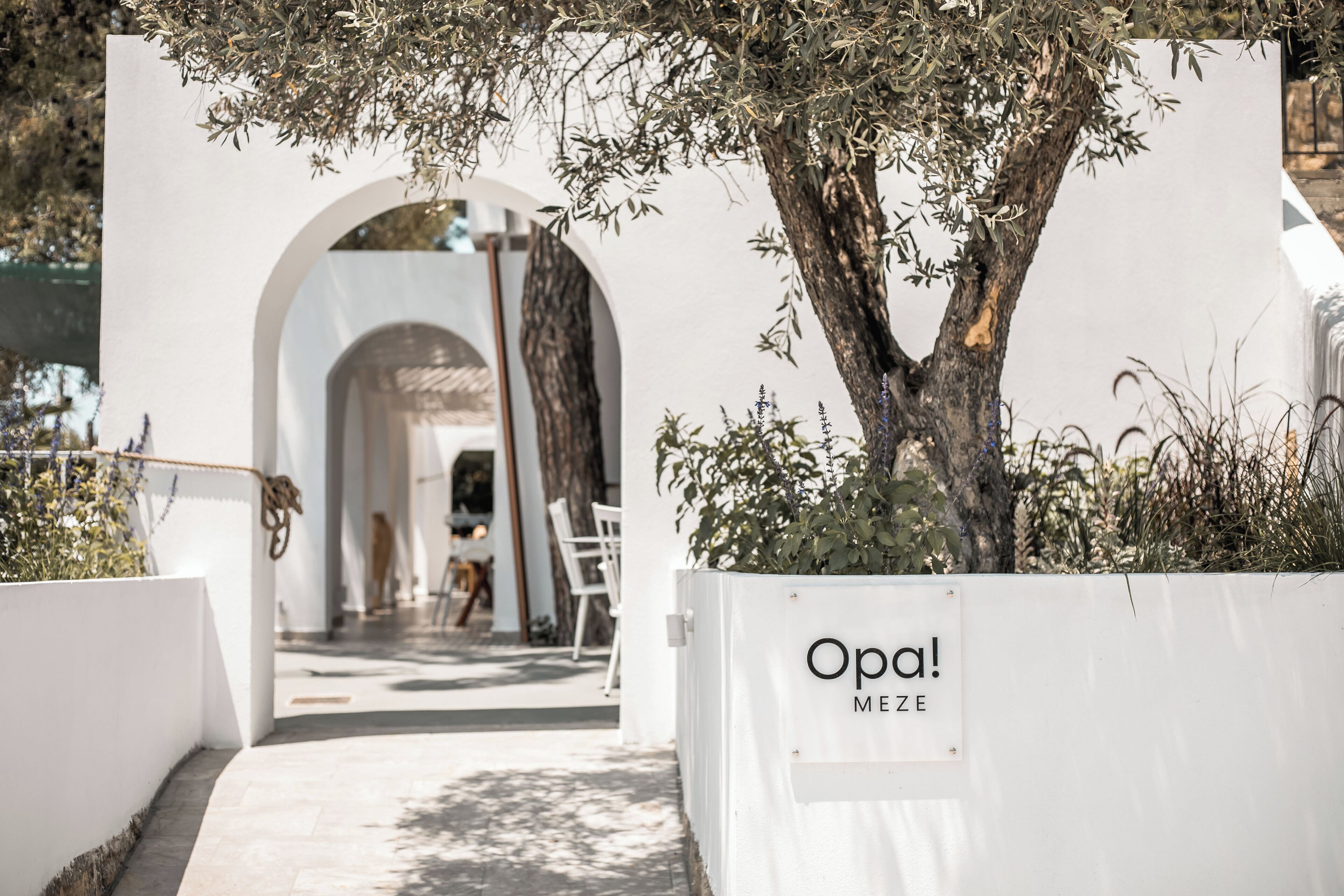 An entrance to a building with a white exterior, an archway, and a sign that reads "Opa! MEZE".