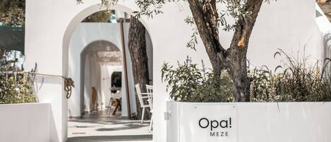 An entrance to a building with a white exterior, an archway, and a sign that reads "Opa! MEZE".