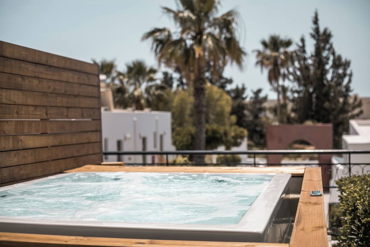 A hot tub with a wooden deck, surrounded by a wooden fence and palm trees.
