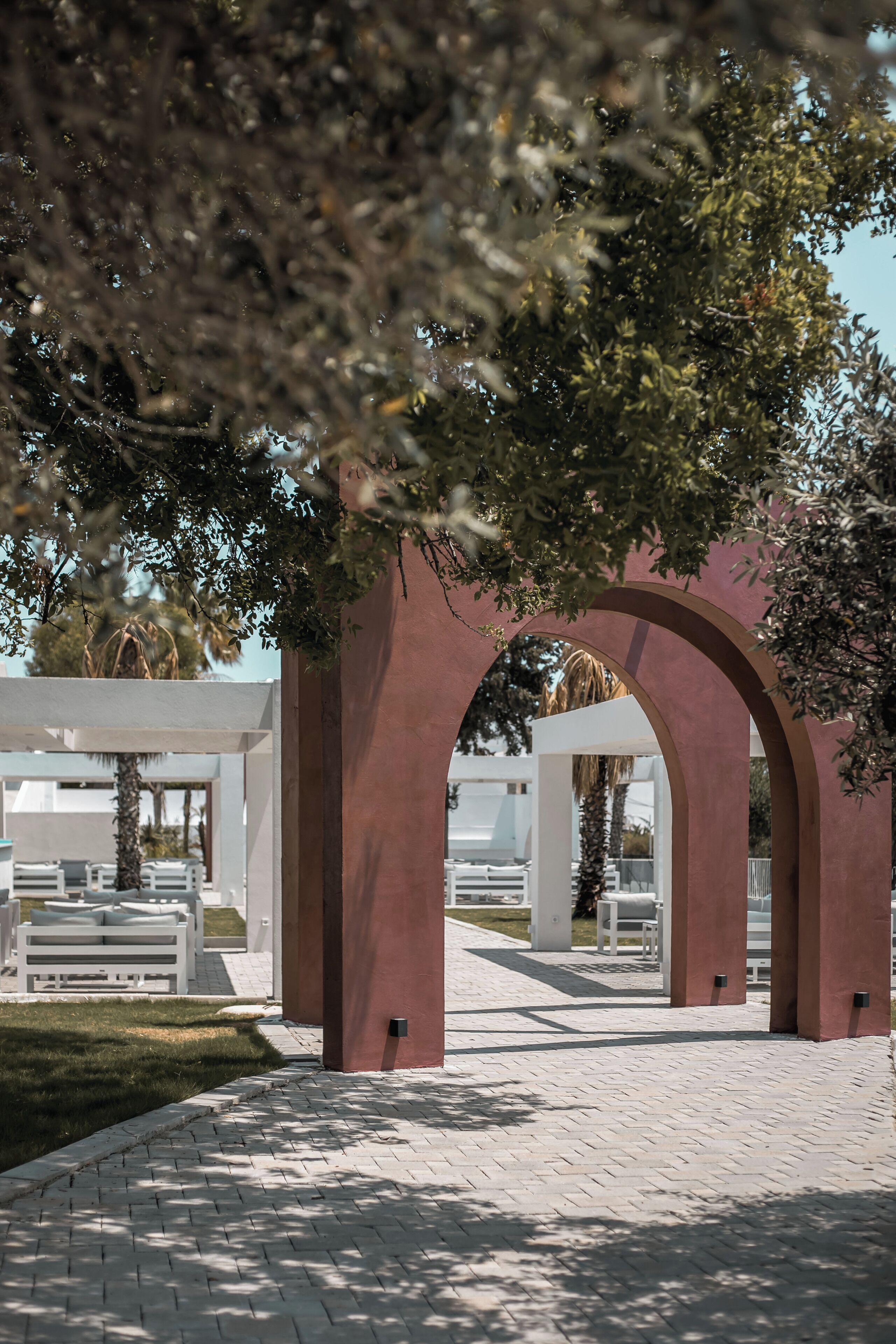 An outdoor pathway with arches, white furniture, and greenery.