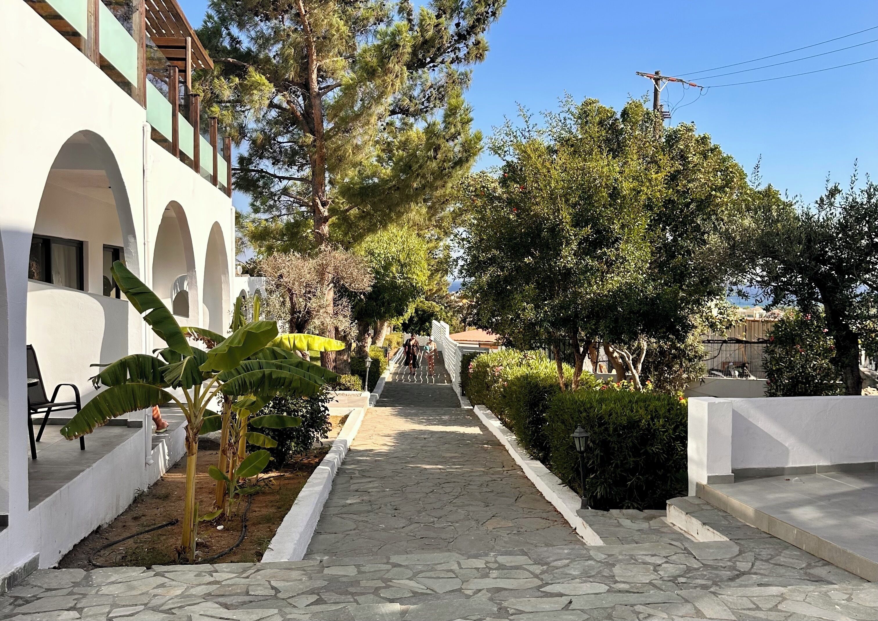 Un camino que lleva a un edificio con arcos blancos y un área techada con sillas.
