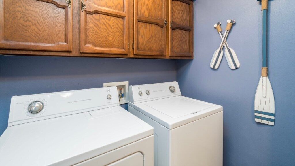 A laundry area with two white washing machines and wooden cabinets above.