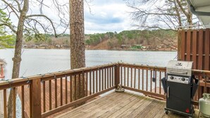 Eine Holzterrasse mit Grill und Propanflasche, mit Blick auf einen See und Häuser im Hintergrund.