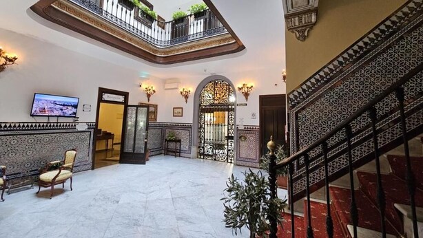 Eine geräumige Lobby mit hoher Decke, einer Treppe mit kunstvollen Geländern und einem Balkon mit Pflanzen.