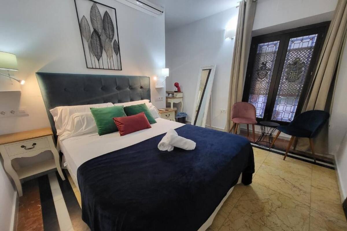 Hotellihuone, jossa on sänky, yöpöytä, tuoli, peili ja ikkuna, jossa on verhot.