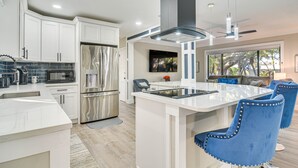A modern kitchen with white cabinetry, stainless steel appliances, and a central island with blue chairs. - Serene St Petersburg Home w/ Private Hot Tub (St. Petersburg)
