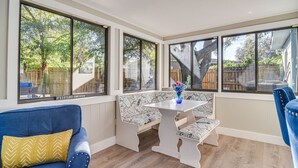 A sunlit room with large windows, a blue sofa, a white bench, and a table with a vase. - Serene St Petersburg Home w/ Private Hot Tub (St. Petersburg)