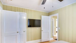 A bedroom with two white doors, a flat-screen TV mounted on the wall, and a bed with a white cover. - Augusta Home w/ Fenced Yard - 4 Mi to Downtown! (Augusta)