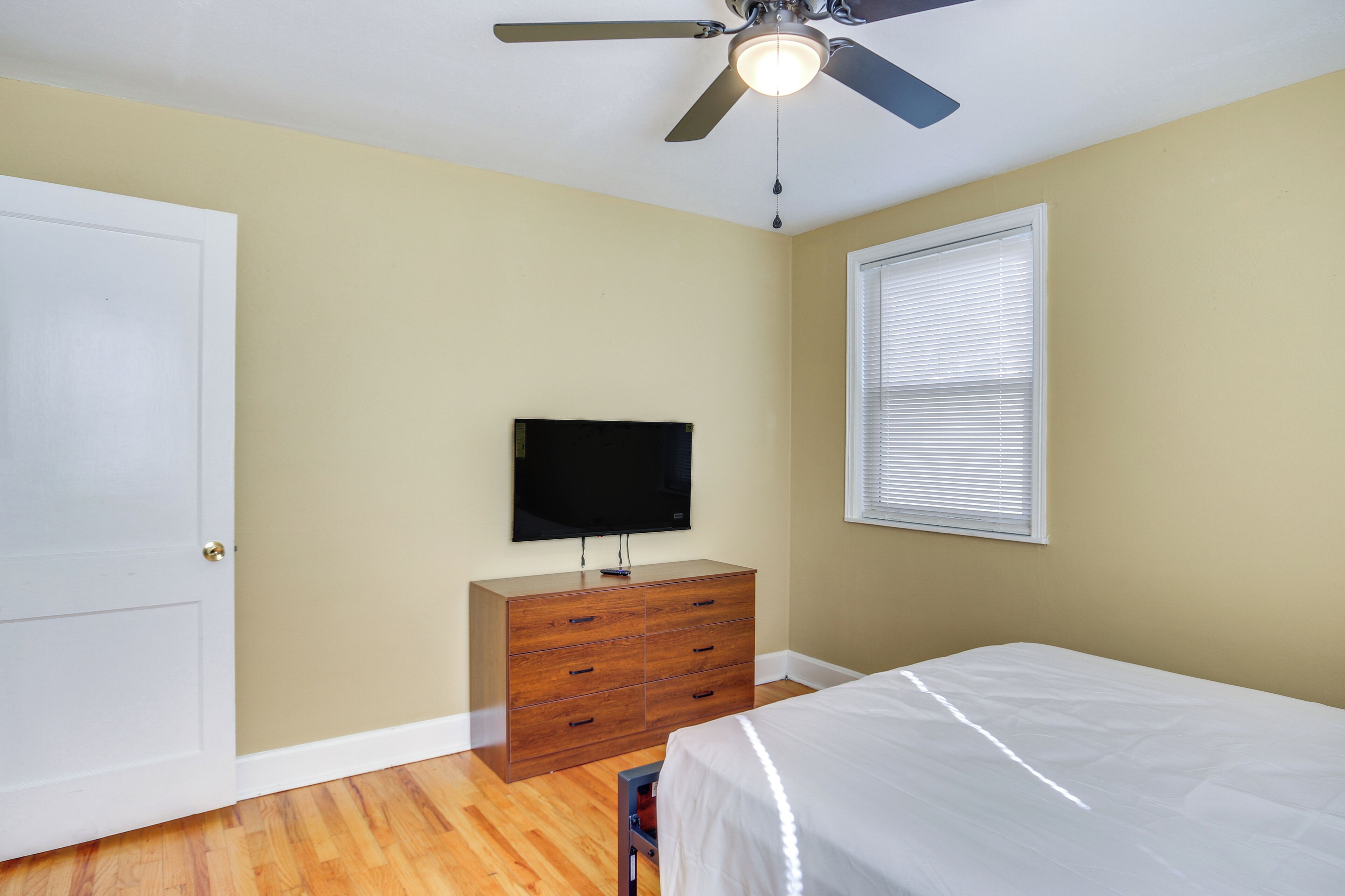 A bedroom with a bed, a dresser, a television, and a ceiling fan.