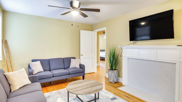 A living room with a sofa, armchair, and a small round table. There is a fireplace with a white mantel and a flat-screen TV mounted above it. - Augusta Home w/ Fenced Yard - 4 Mi to Downtown! (Augusta)