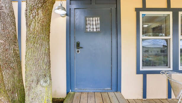Een blauwe deur met een klein raam, een metalen deurbel en een houten terras.