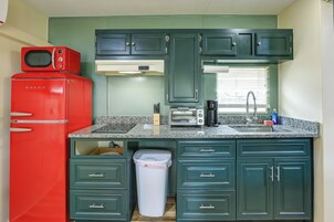 Una cocina compacta con armarios verde azulado, un refrigerador rojo, un microondas y un tostador.