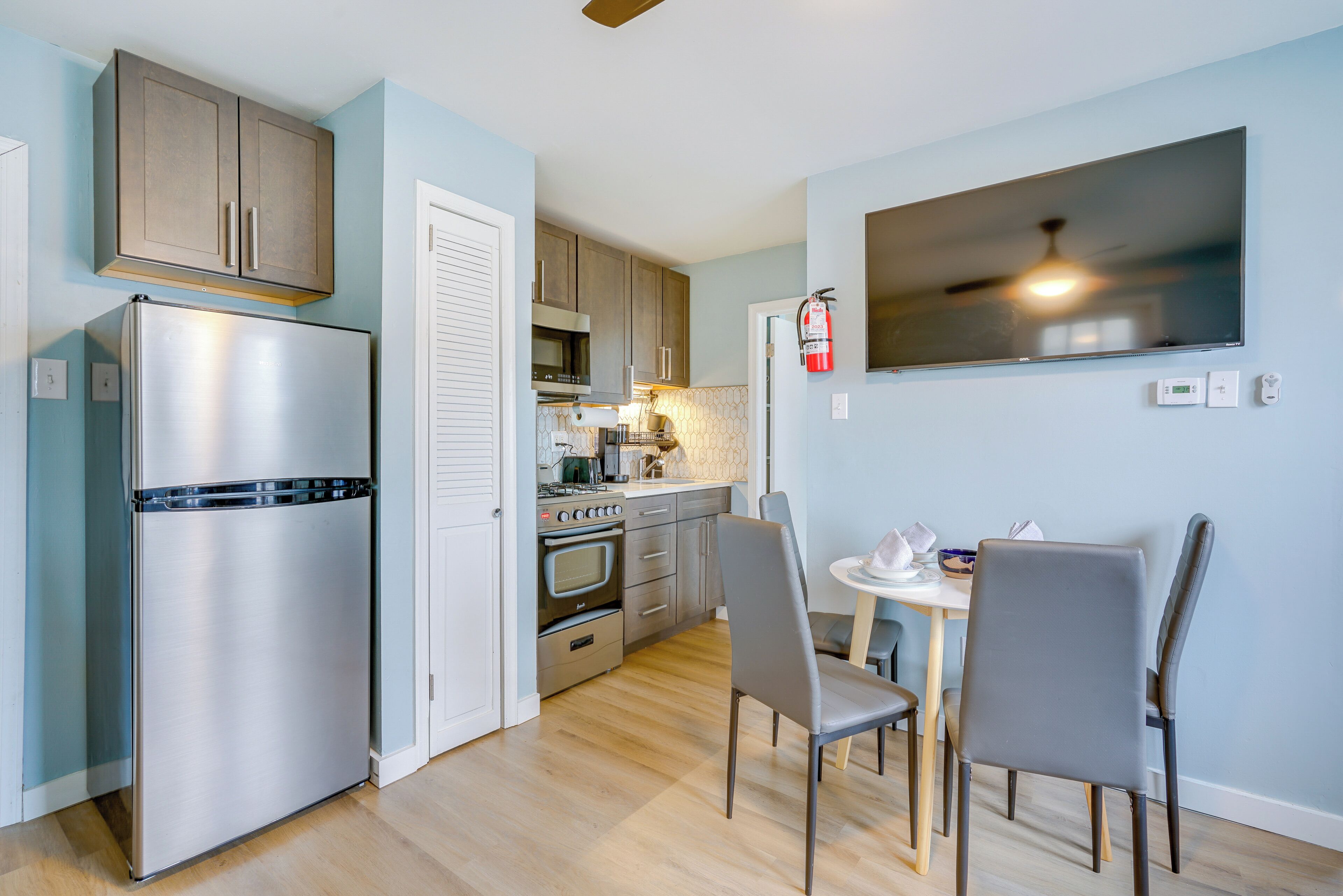 A compact kitchen with a refrigerator, oven, and microwave. There is a dining area with two chairs and a small table.