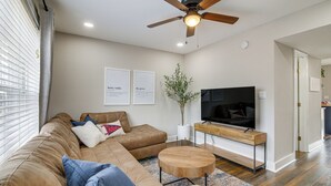 A living room with a brown leather sofa, a wooden coffee table, a TV on a wooden stand, and a ceiling fan.