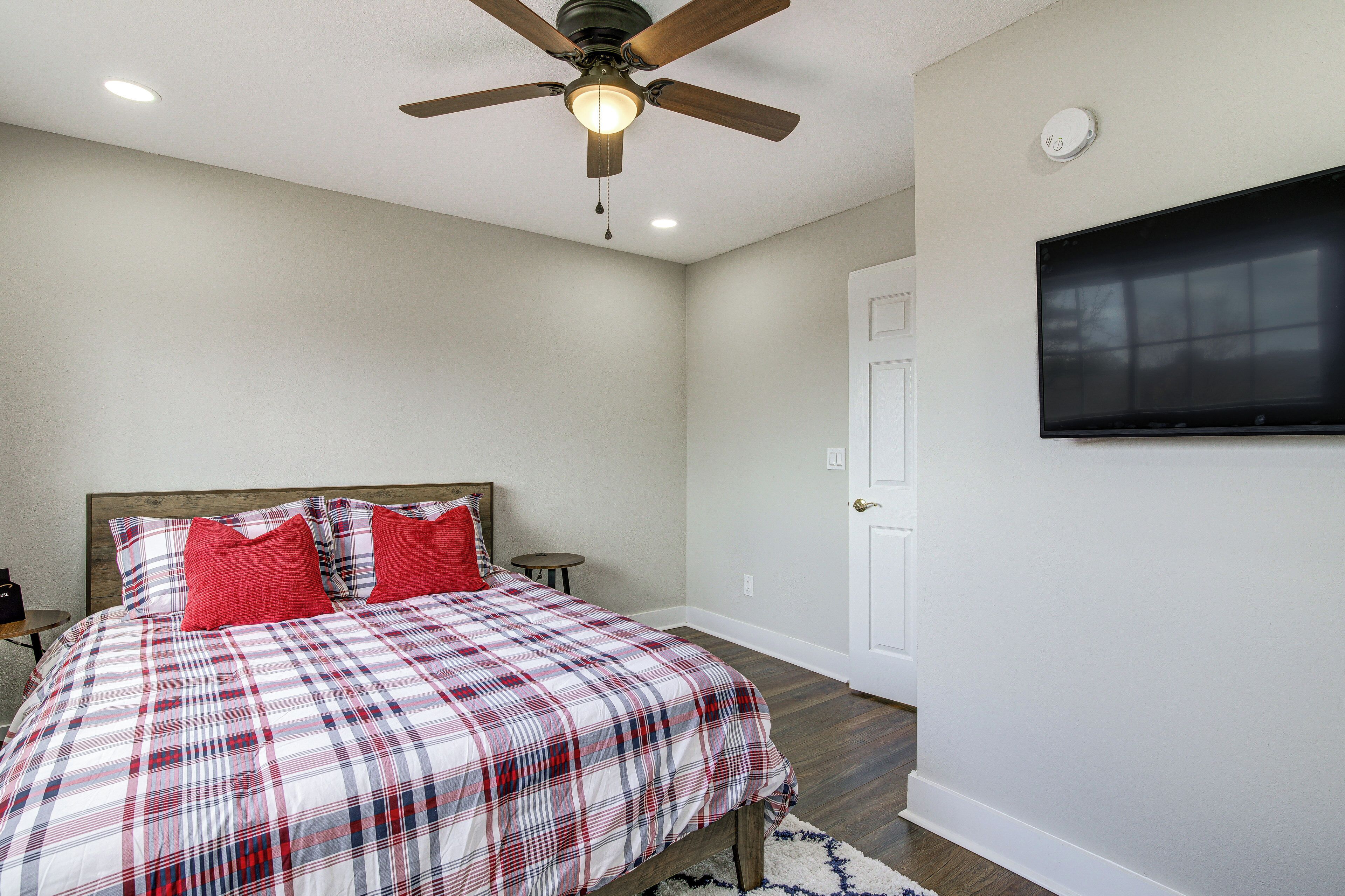 A bedroom with a bed, a ceiling fan, a mounted TV, and a white door.
